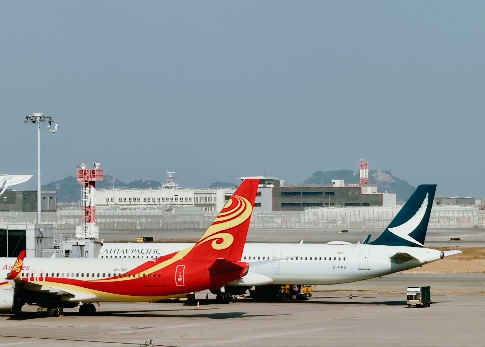 两架飞机停在机场跑道上，一架红色TAILAND AIRLINES，一架蓝色新加坡航空。