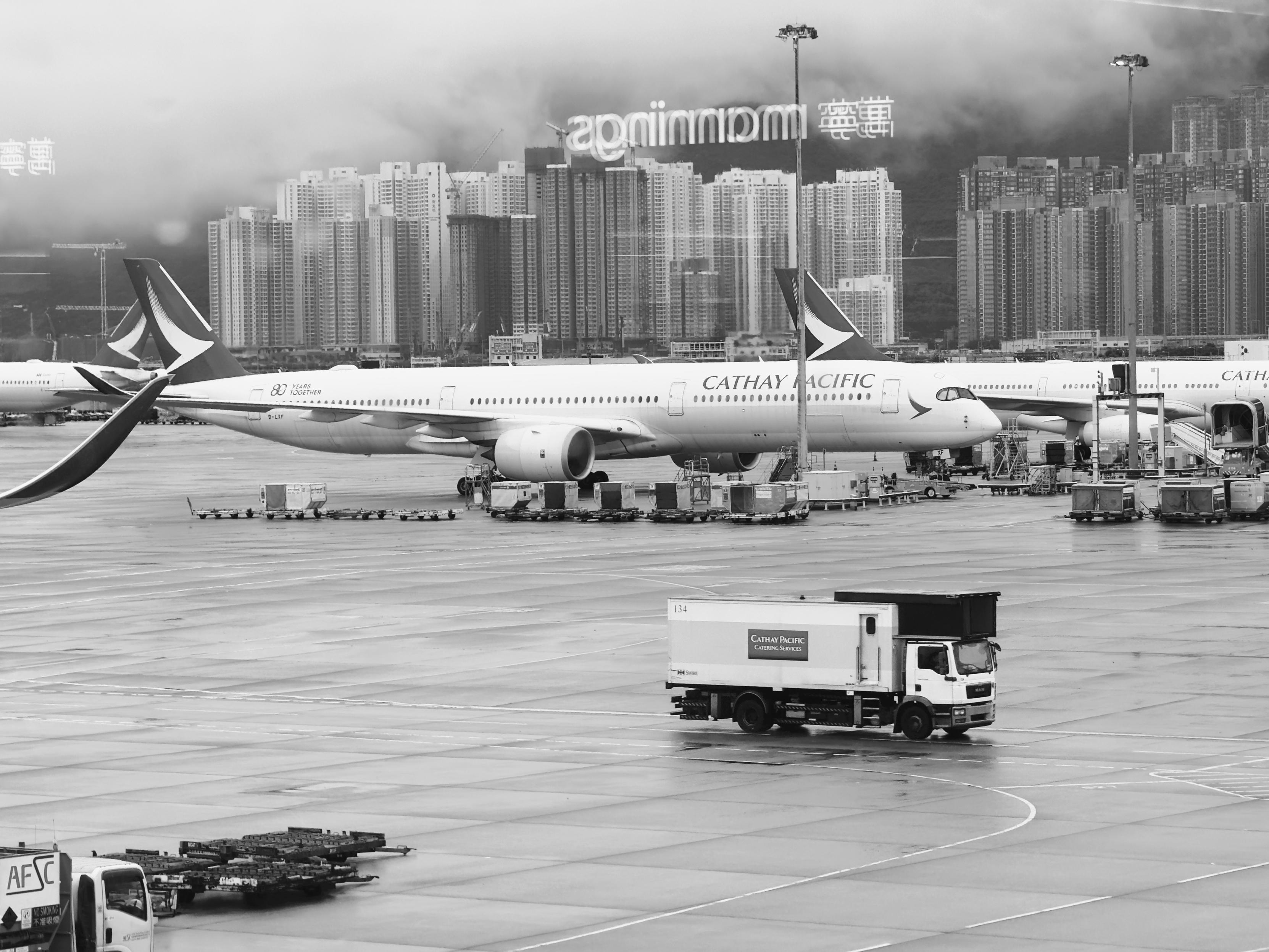 香港国际机场停机坪上，凯旋航空的飞机准备起飞，背景为高楼林立的城市天际线。