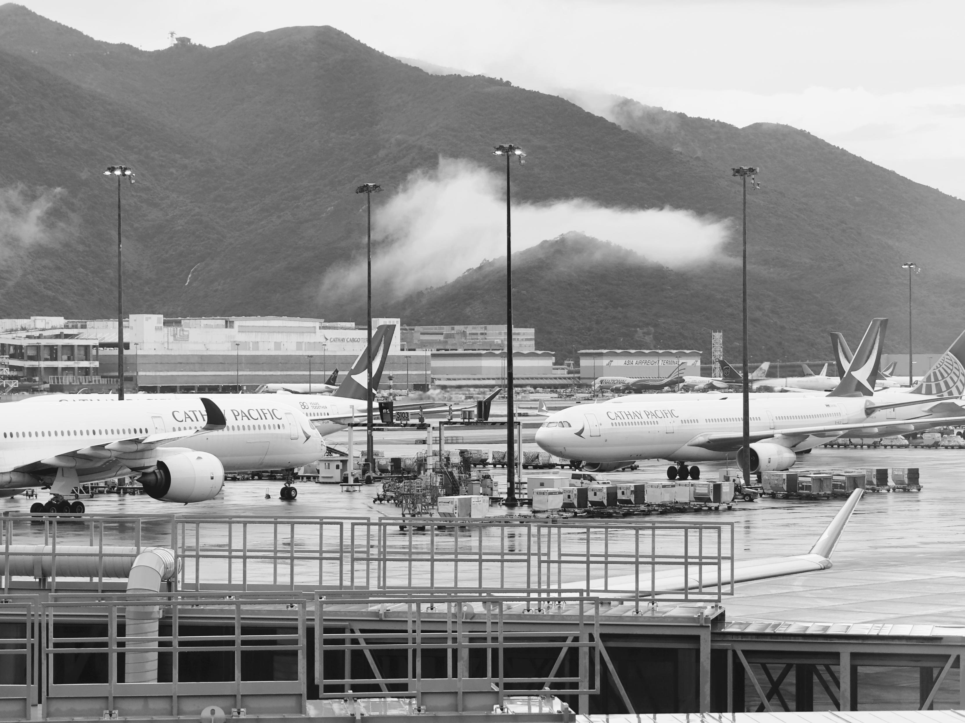机场停机坪上有多架国泰航空飞机，背景是山脉和云雾。