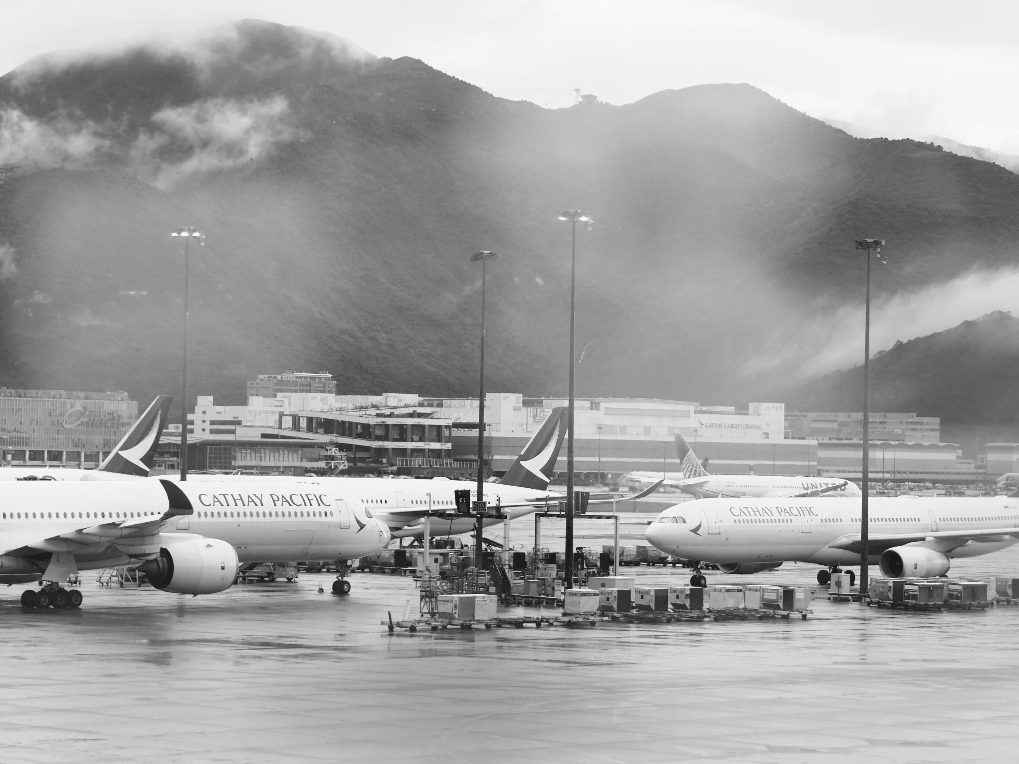 香港国际机场停着几架国泰航空的飞机，背景是云雾缭绕的山峦。