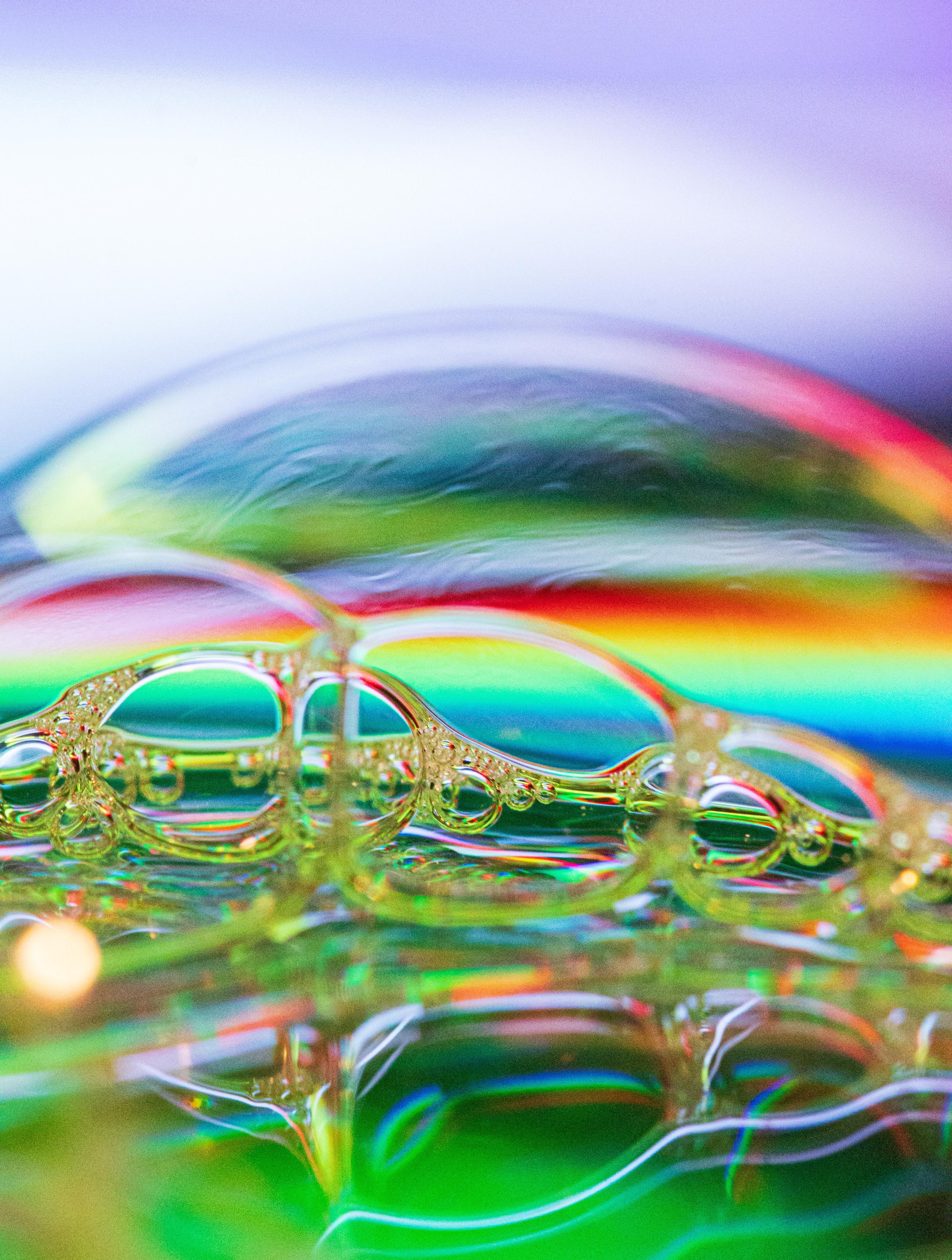 A macro photo of soap bubbles underneath an led light. They are in various shades of neon and very bright.