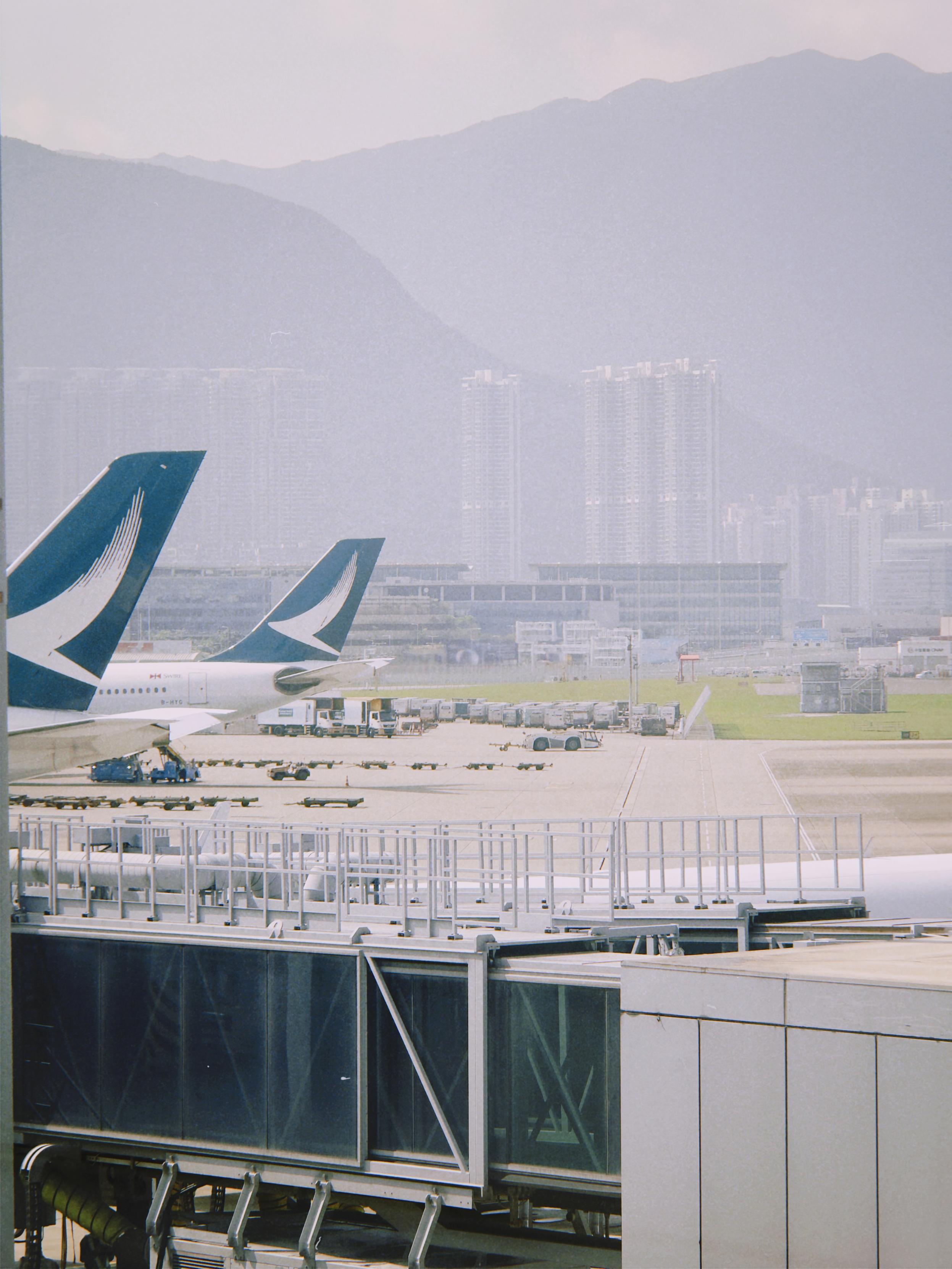 Airplanes parked at a terminal with mountains and city buildings in the background.