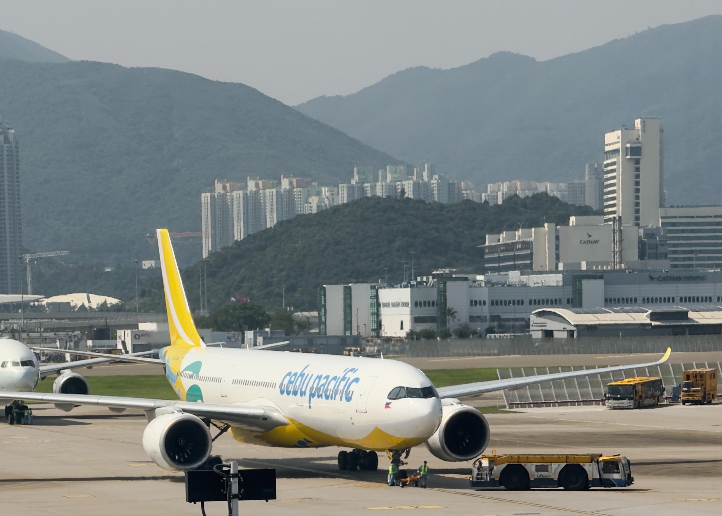一架亚洲航空A320飞机停靠在机场跑道上，背景是山脉和城市高楼。