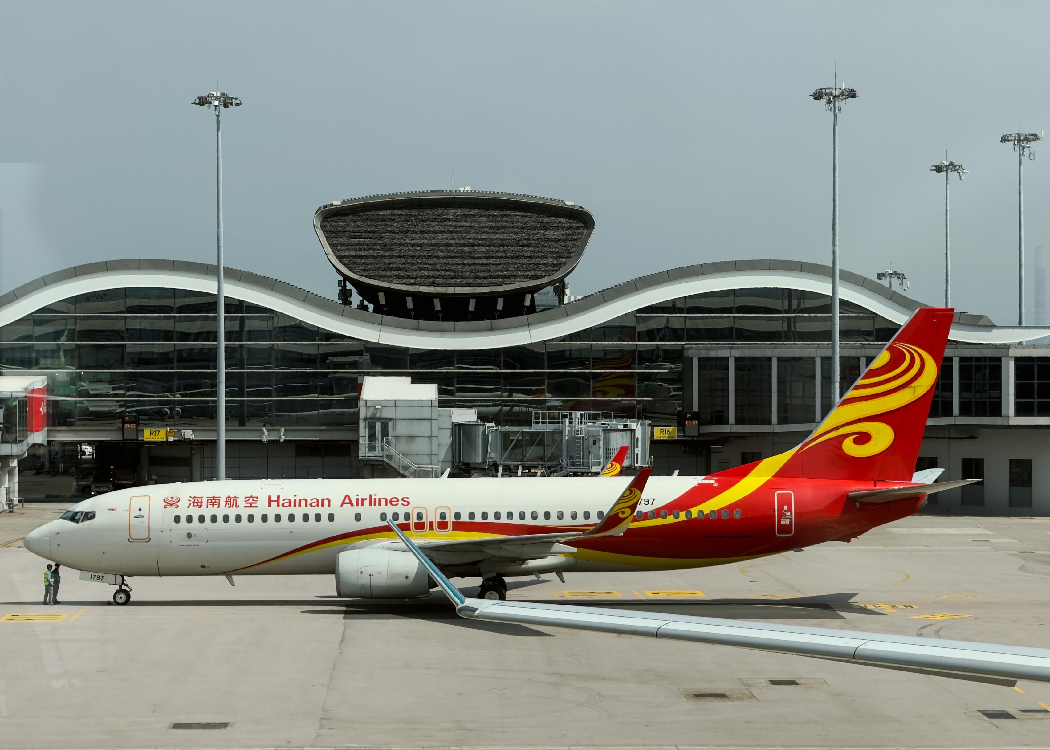 海南航空喷气式客机停在机场跑道上，背景是现代建筑和登机门。