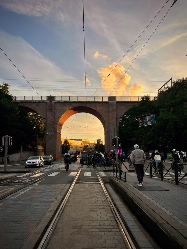 Wagon, Uccle, Brussels-Capital, Belgium

A brick viaduct arches over a paved road and tram tracks at sunset. The sky is painted with warm hues of orange and yellow clouds against a blue backdrop. Pedestrians walk along the towpath on either side as cyclists ride beneath the bridge. Utility poles with wires stretch across the scene, and trees line both sides of the road.

35 mm equivalent: 26 mm