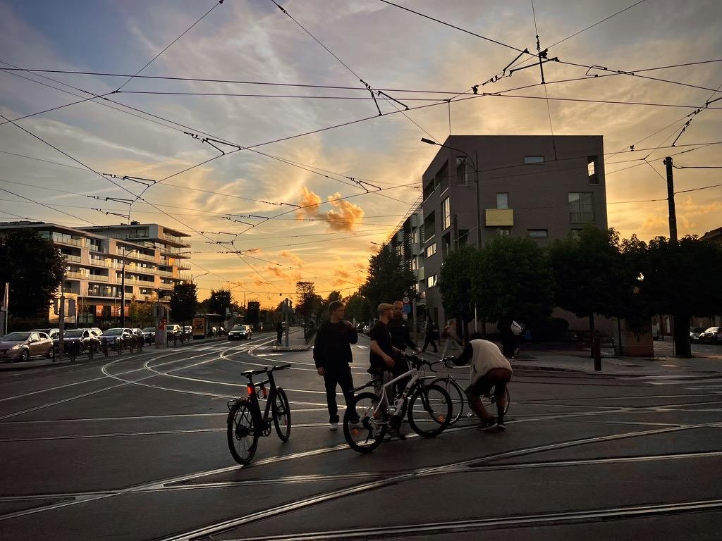 AtriaTECH Uccle, Uccle, Brussels-Capital, Belgium

At sunset, cyclists and pedestrians gather on a paved road with tram tracks, under overhead wires against a sky painted in warm hues of orange and yellow. Modern buildings line one side while trees frame the other, casting long shadows across the scene. A parked houseboat is visible near some trees to the right.

35 mm equivalent: 26 mm