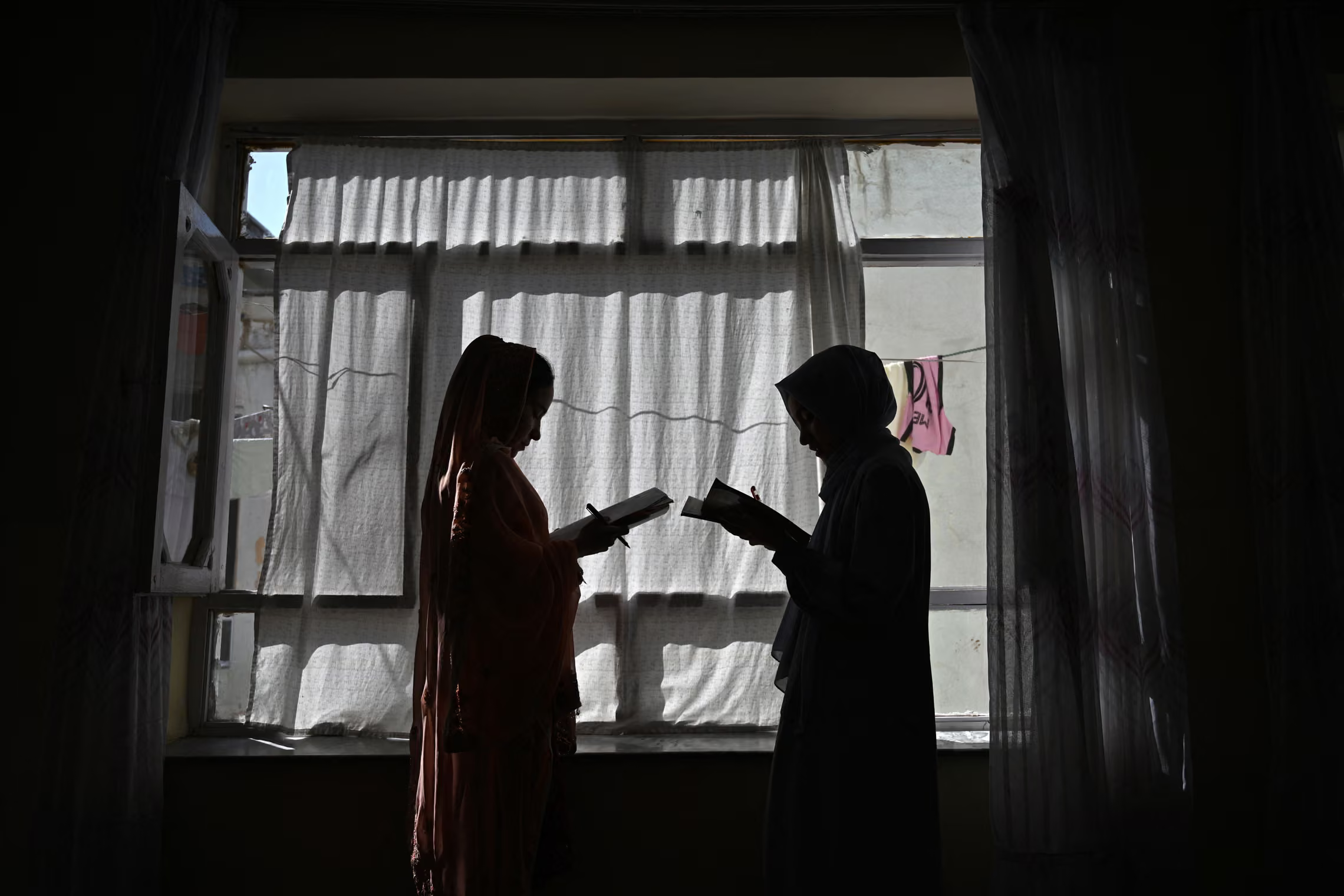 Two girls read books in a twilight by the window.
