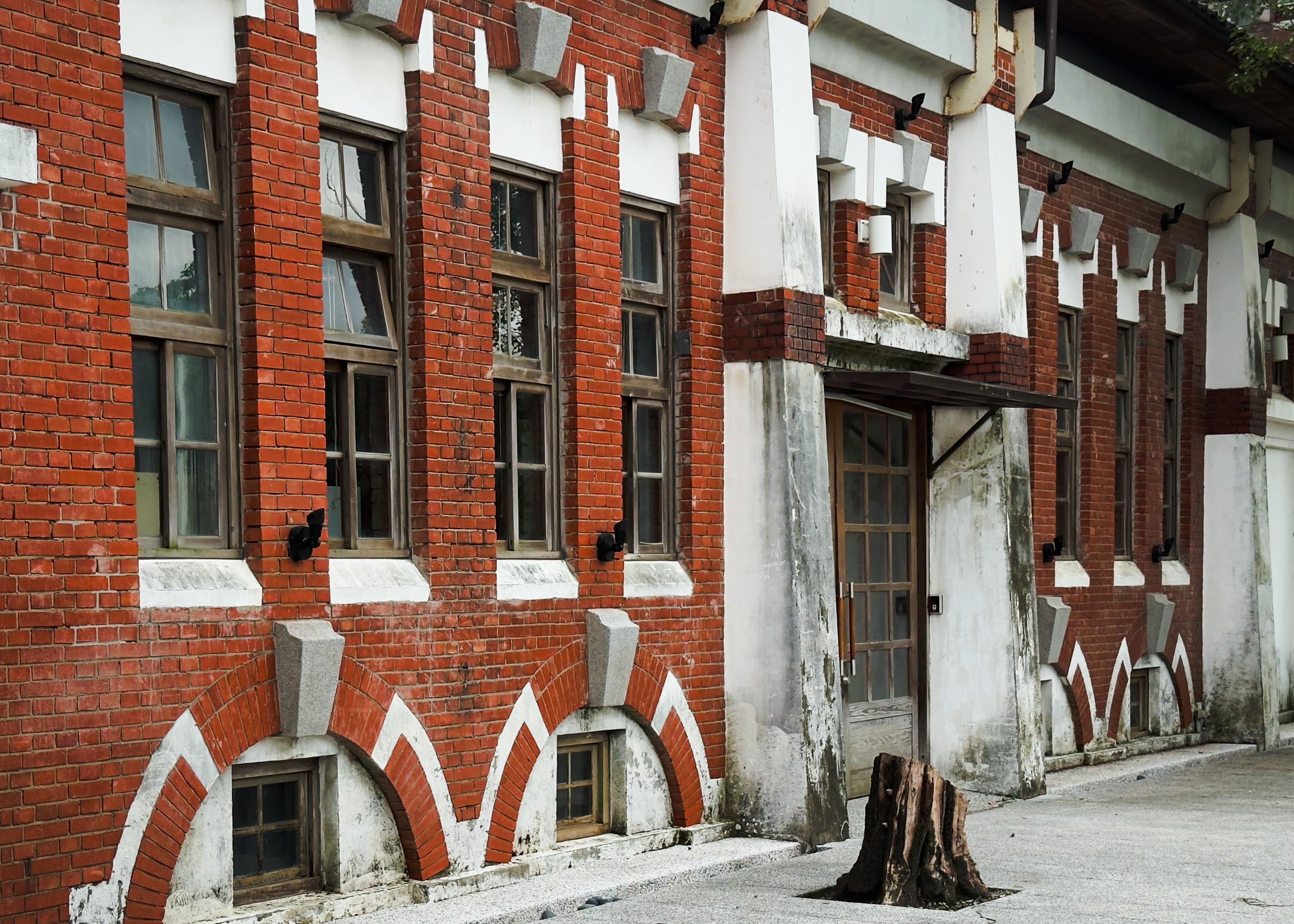 一座红砖建筑，有多个窗户和门，带有白色和灰色装饰，墙壁略显陈旧。