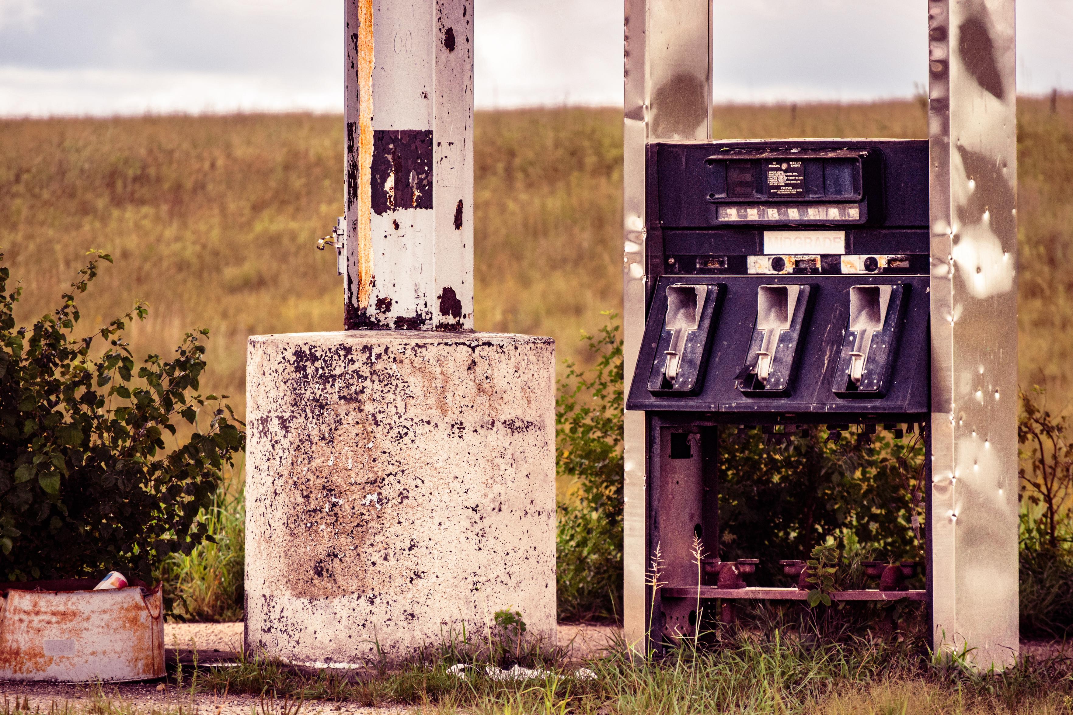Weathered vintage gas pump stands between peeling white posts in an overgrown rural field, evoking abandonment and faded nostalgia.