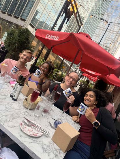 Four people at a restaurant dinner table holding coffee mugs branded with Djangonaut space logo smiling for the photo 