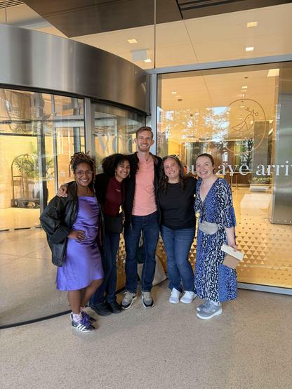 Five people standing outside a hotel posing for the camera smiling 