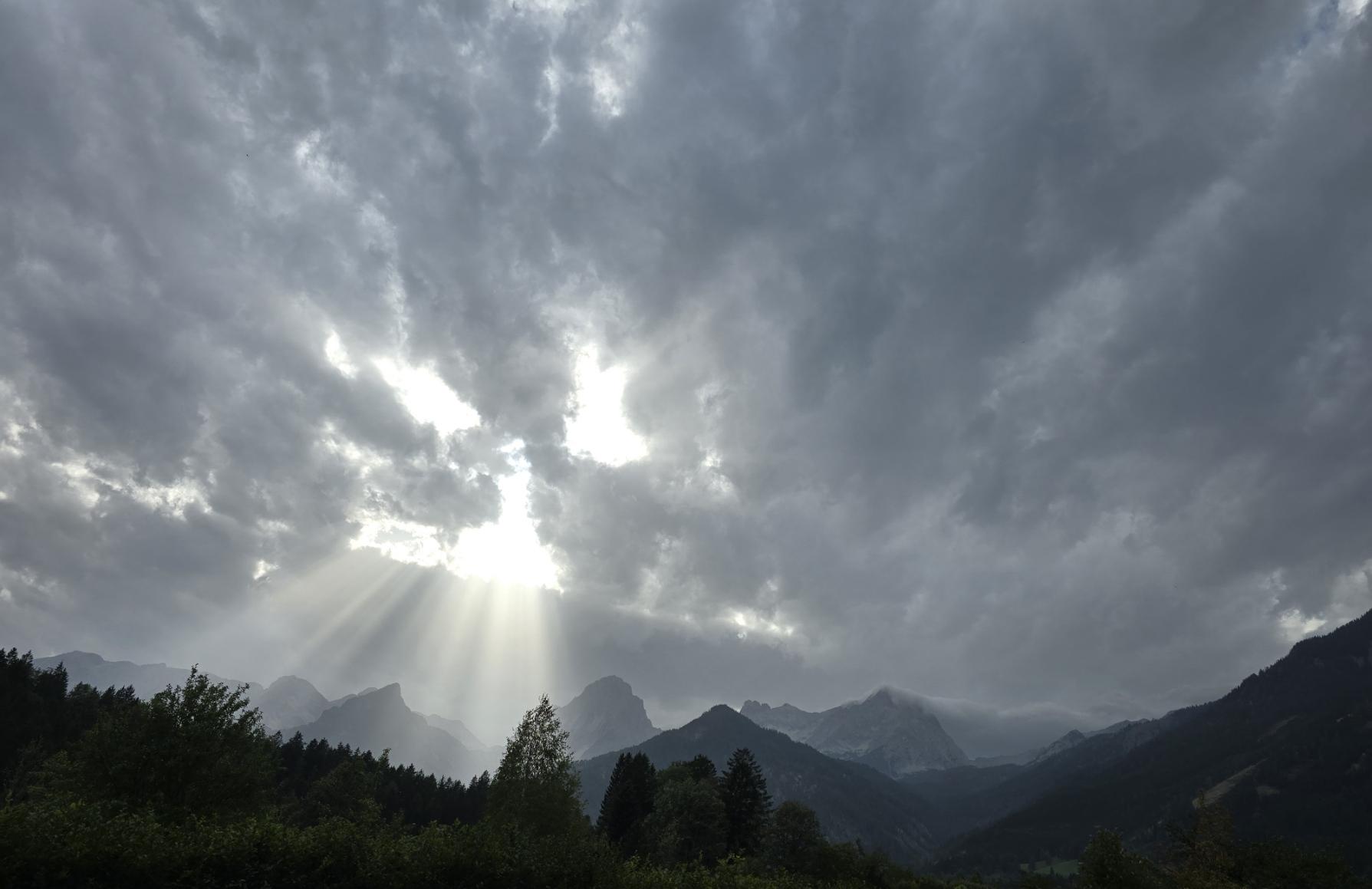 Eine Stunde vor Sonnenuntergang. Alpen. Volle, dunkle, schwere Wolken lassen keine Sonne durch. Durch 3 Löcher, die wie ein Gesicht aussehen, fallen intensive Sonnenstrahlen.