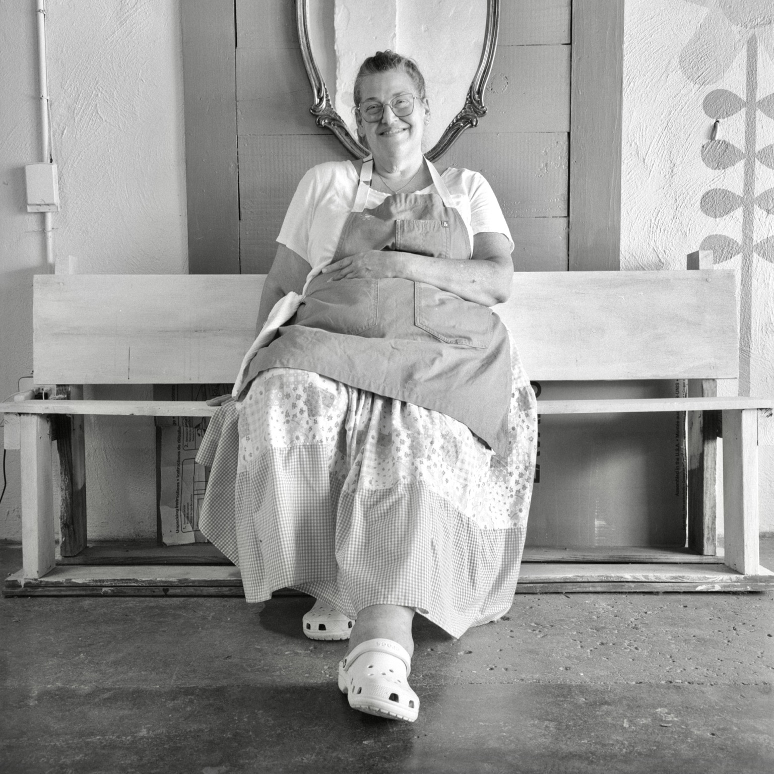 A black-and-white film photo. Kim is seated on a bench in her wonderful bakery in Lexington, Texas. Friday, August 14, 2026.