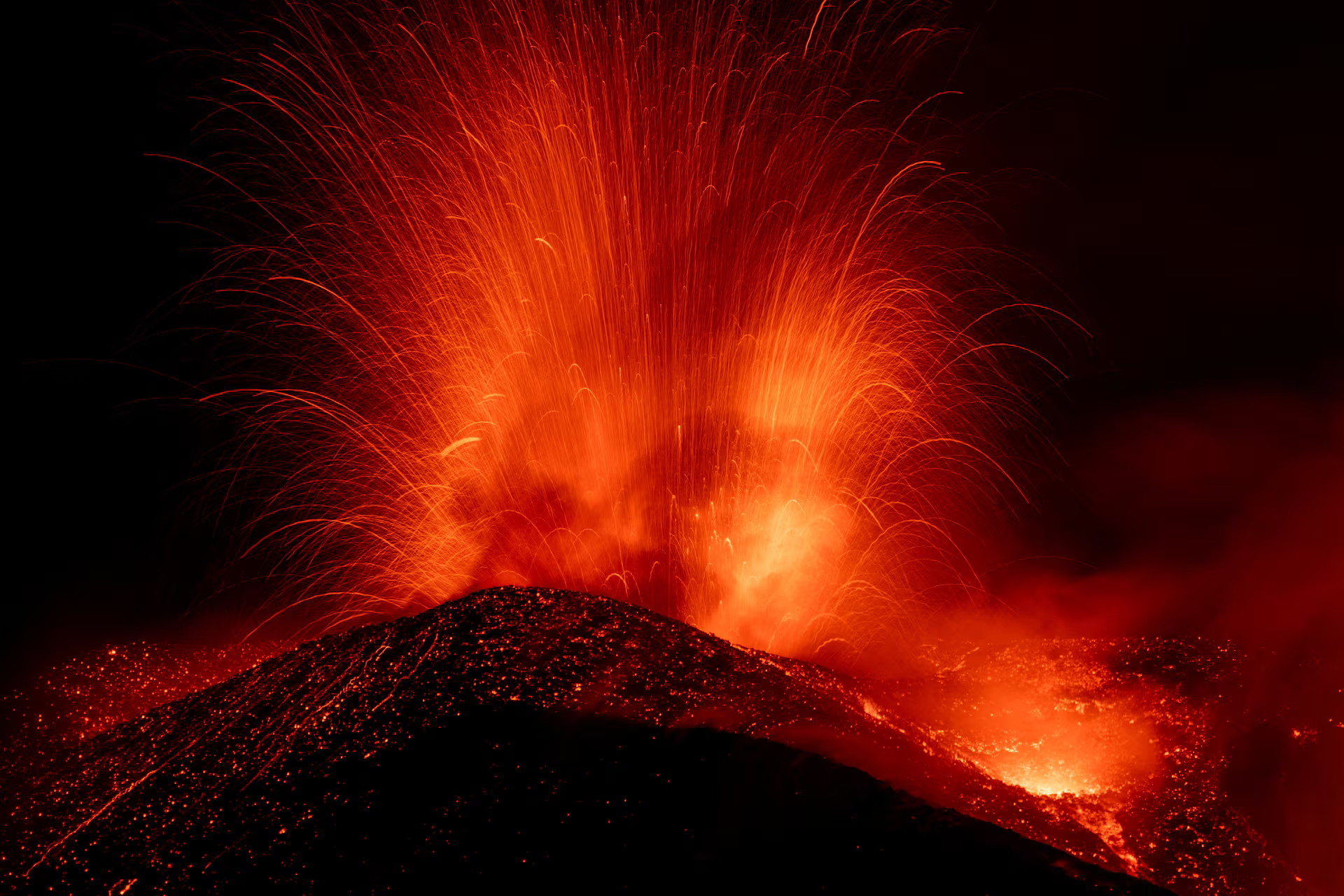 Incandescent lava and volcanic material are ejected from a crater during an eruption of Mount Etna at night.