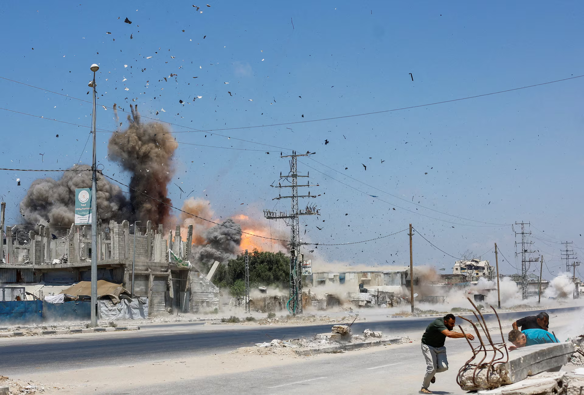 People run for cover as debris flies through the air during an Israeli strike.