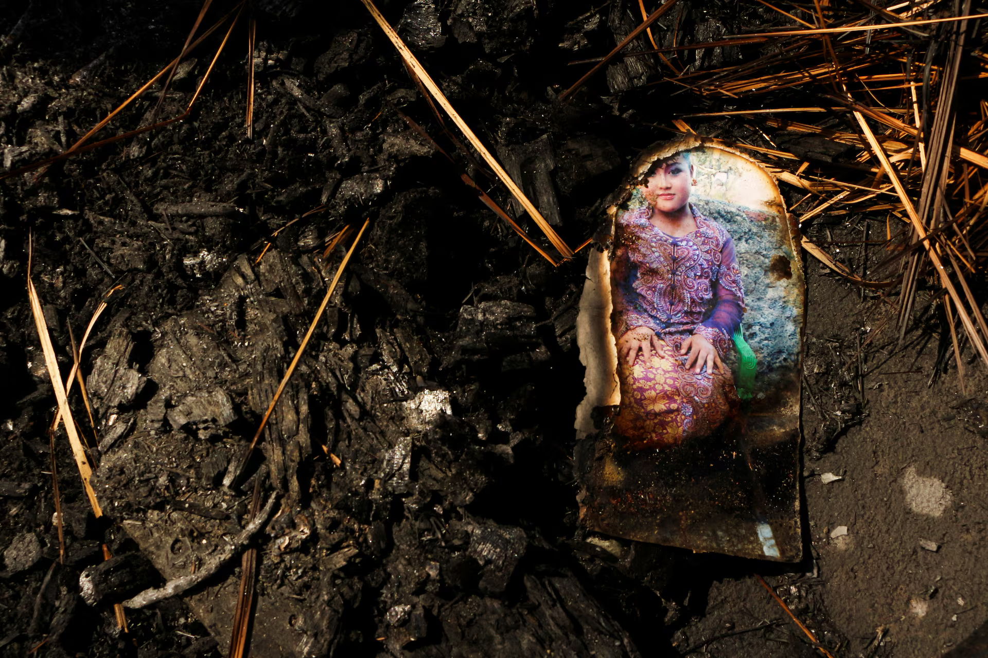 A portrait of a woman wearing traditional clothes lies on the ground in a burnt house.