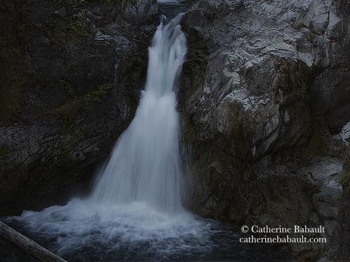 A tall waterfall rushing down a grey rock face. The photo is dark because it was early in the morning.
