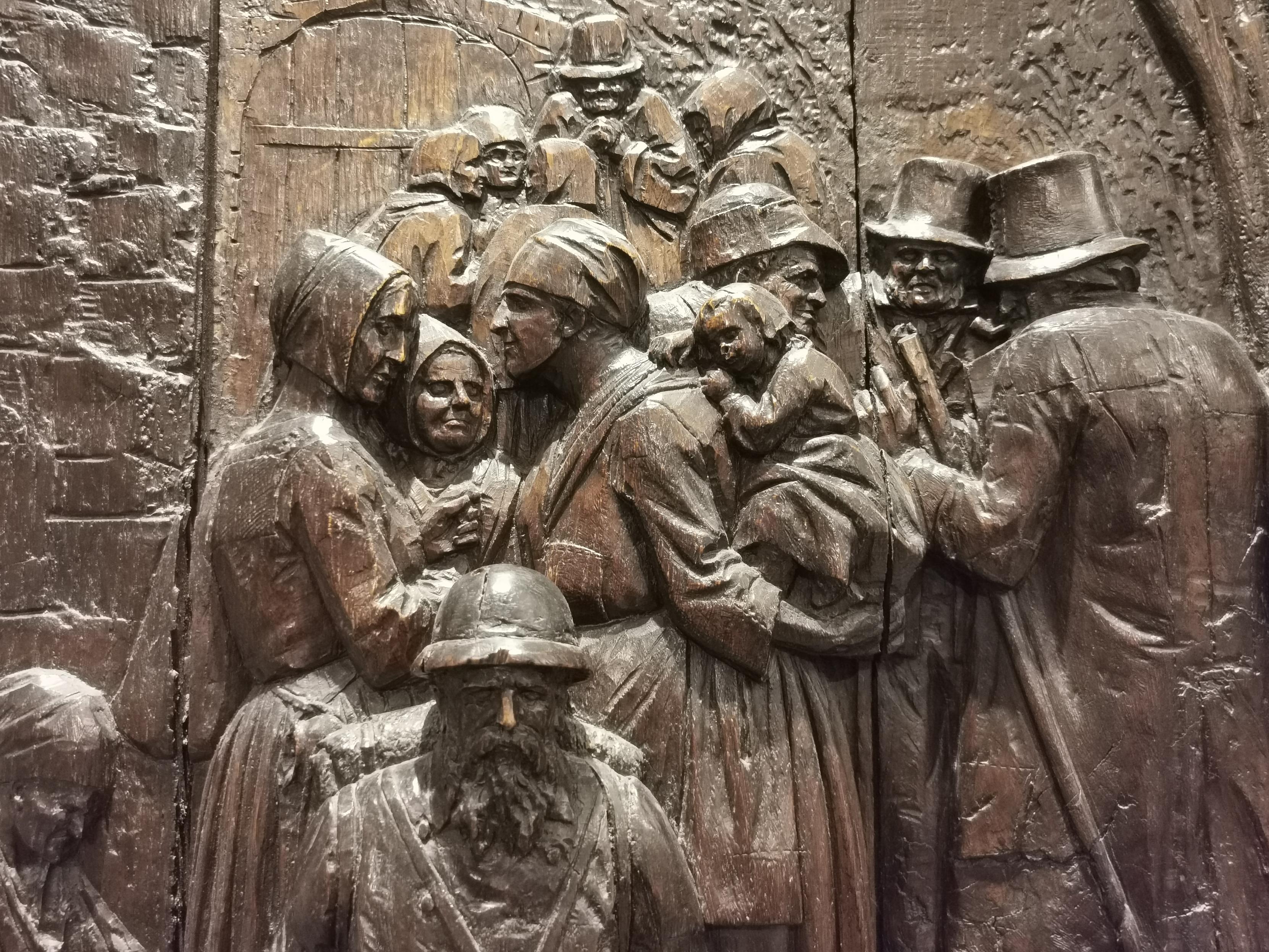 Sculpture sur bois présentant une scène quotidienne avec de nombreux personnages.