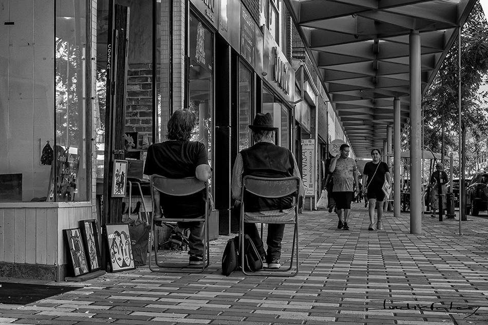 @ people sitting on folding chairs, in front of their small shop, seemingly waiting for customers.