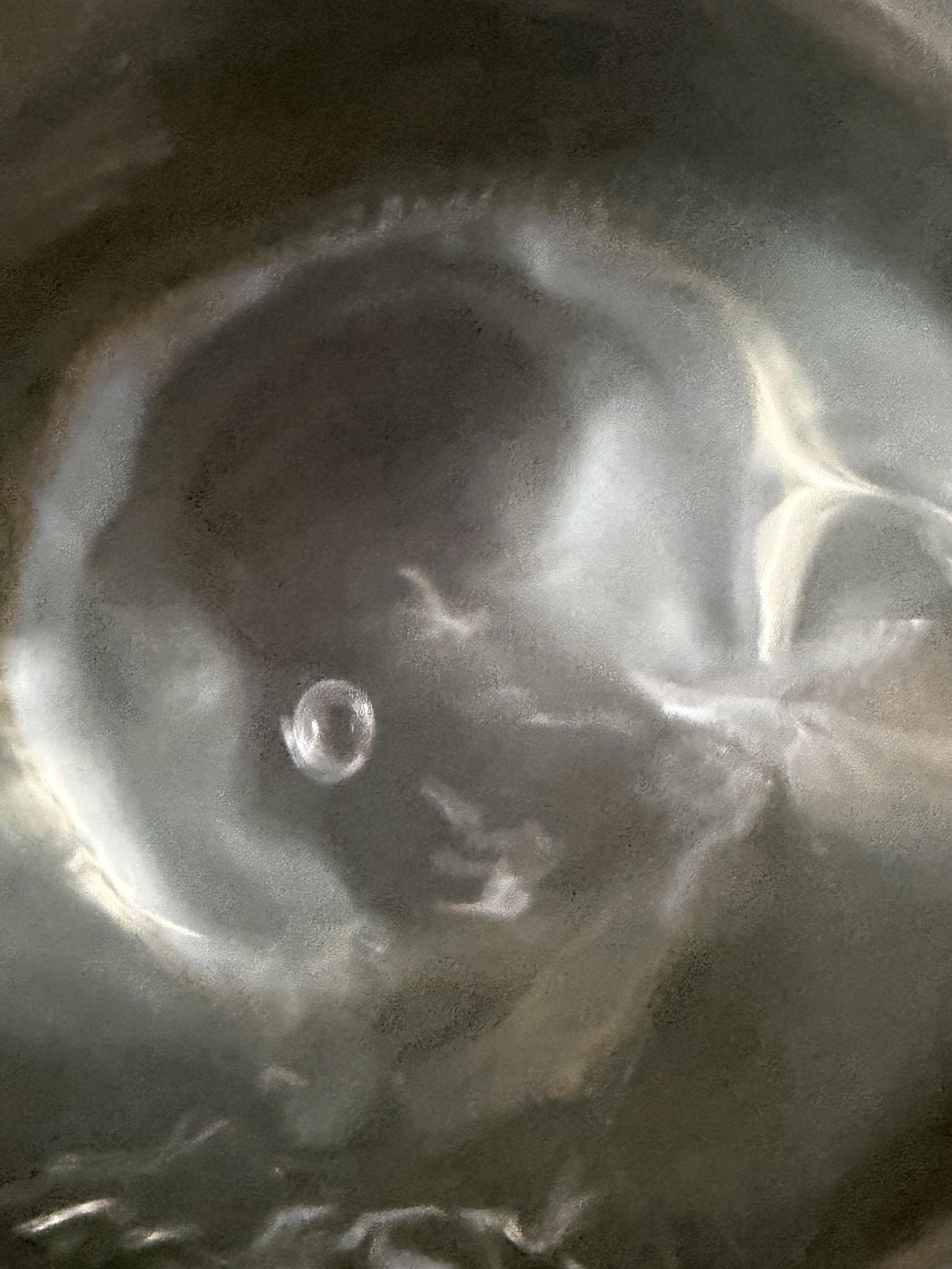 Close-up of water gathered around a small bubble. Light and shadow move across the dark surface, while the curved water holds a brief, translucent shape.
