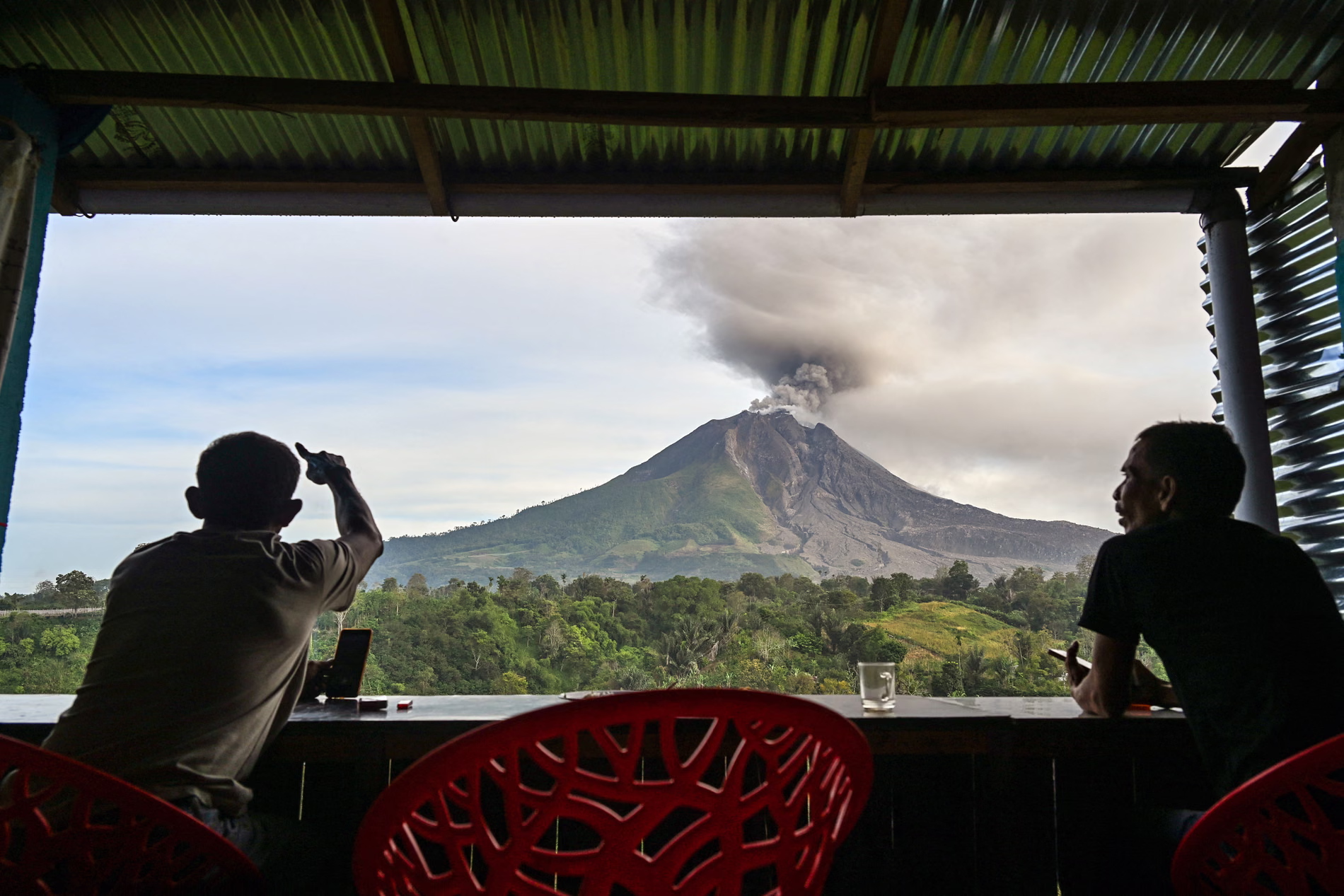 Villages watch a volcano eruption from inside a room with panoramic window.