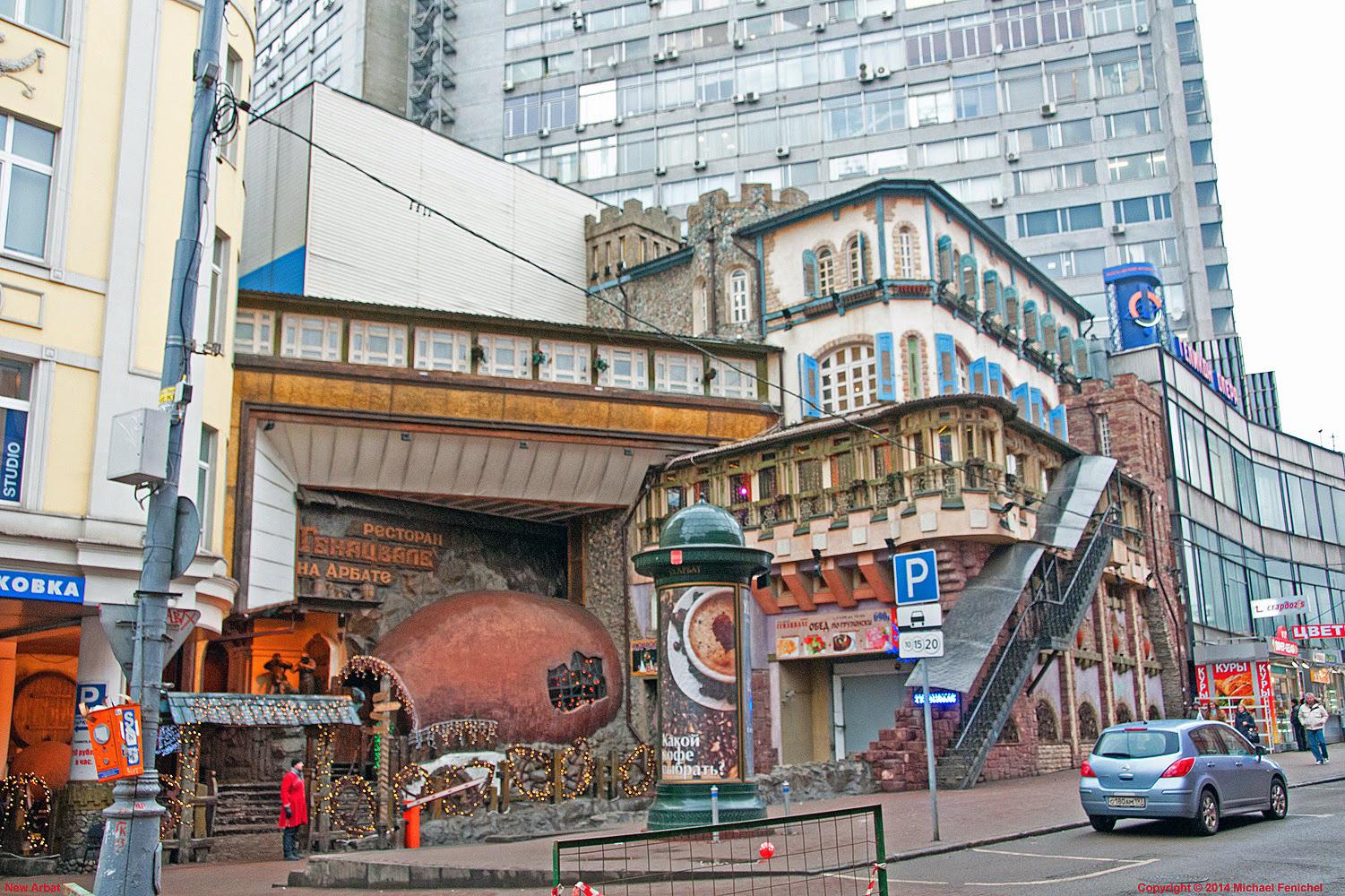 Photo by Fenichel: Old Arbat (Moscow)

A slice of the fabled shopping center in Moscow (Russian Federation)
At the top is a conventional apartment complex looming above the 4-5 story buildings below. From ground level looking ahead, there are some people on th sidewalk (left and right), a large green kiosk with poster (c3nter), stret signs and a passing automobile. The tops of the buildings are asymmetrical, some curved, some in acute angles to each other. In the center, bottom, just left of the green kiosk, is an orange, spherical building facade which defies further description.