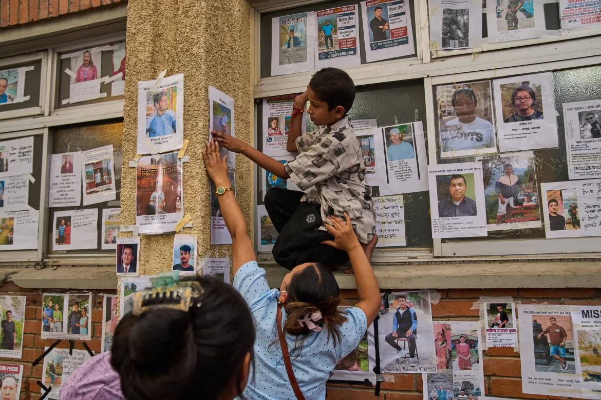 A woman helps a boy put up a photograph of her missing relative on a wall lined with images of missing and deceased people.