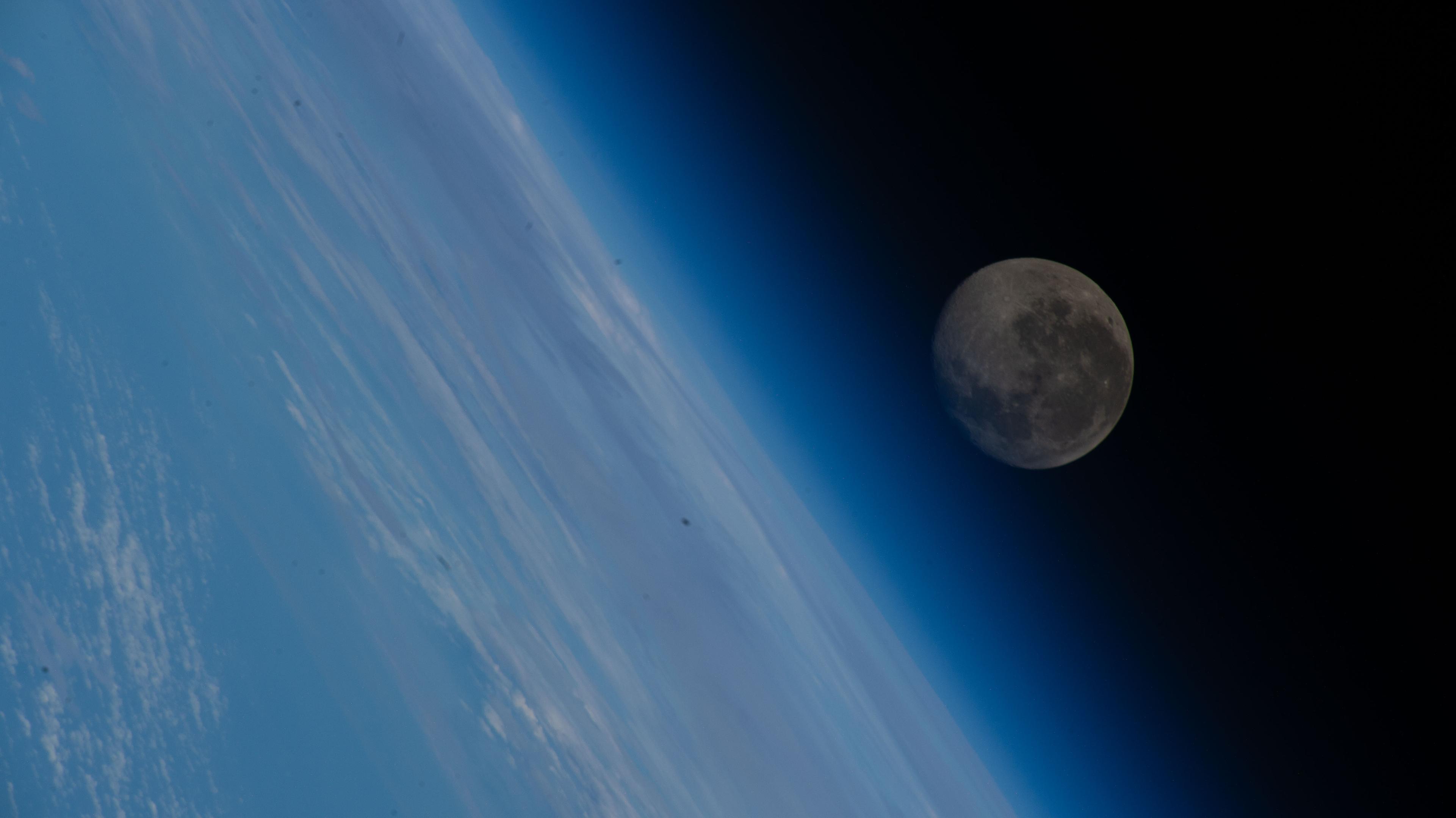 A blue toned image capturing the Moon above Earth's atmosphere as seen from the ISS.