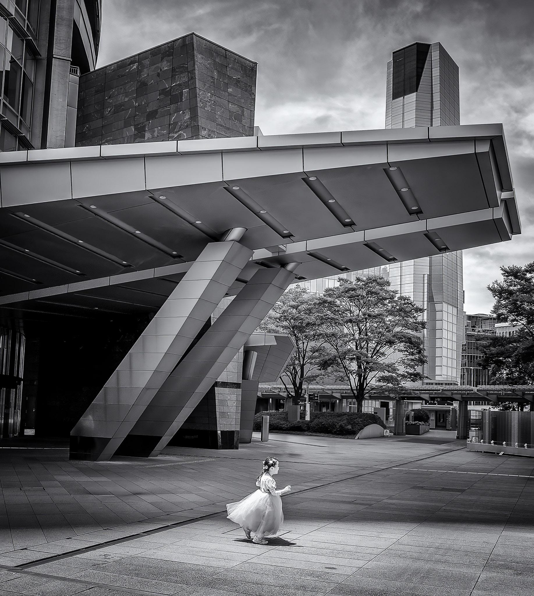 Young girl in a princess costume runs across the courtyard in front of an office building in Tokyo, Japan.