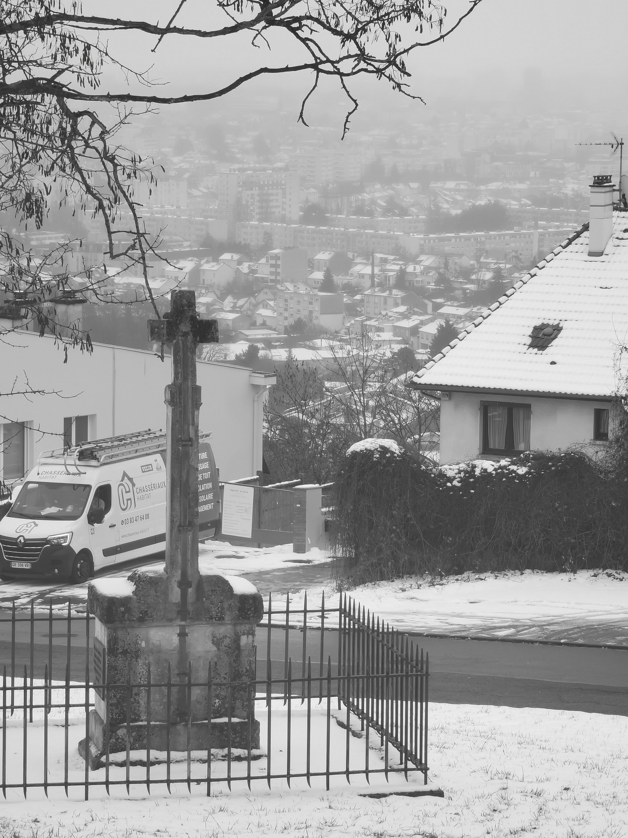 Derrière un calvaire sur les hauteurs s'étale Nancy enneigée dans la cuvette où se trouve la ville.