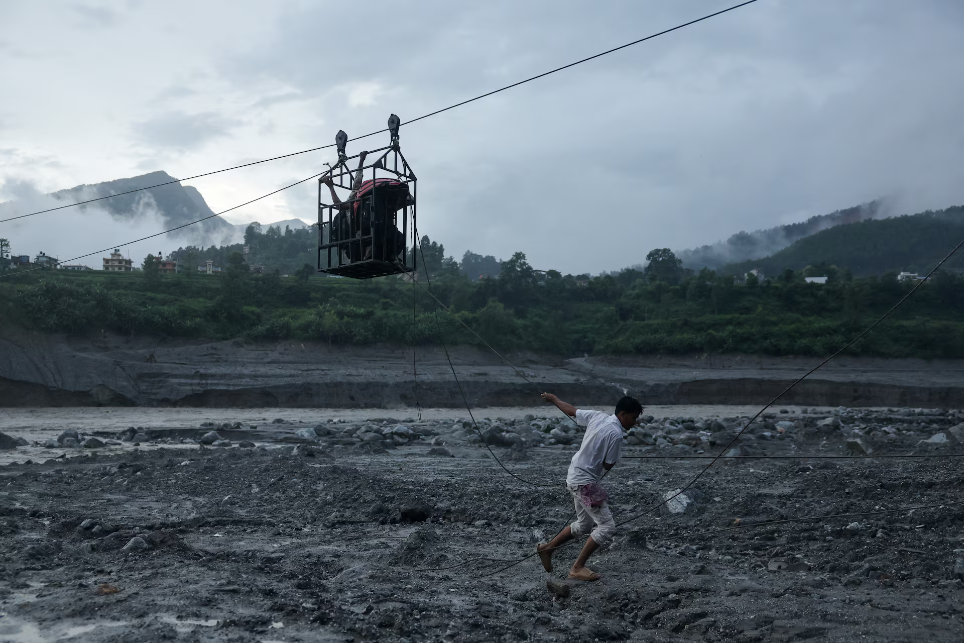 A man pulls a makeshift zip line carrying people across the Trishuli River.
