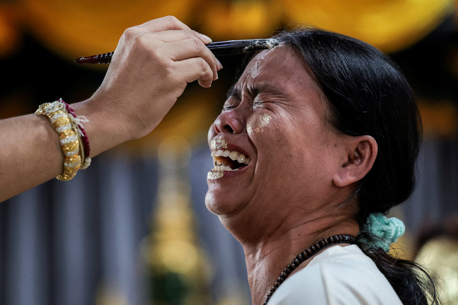 A devotee reacts while gold leaves are applied on her face.