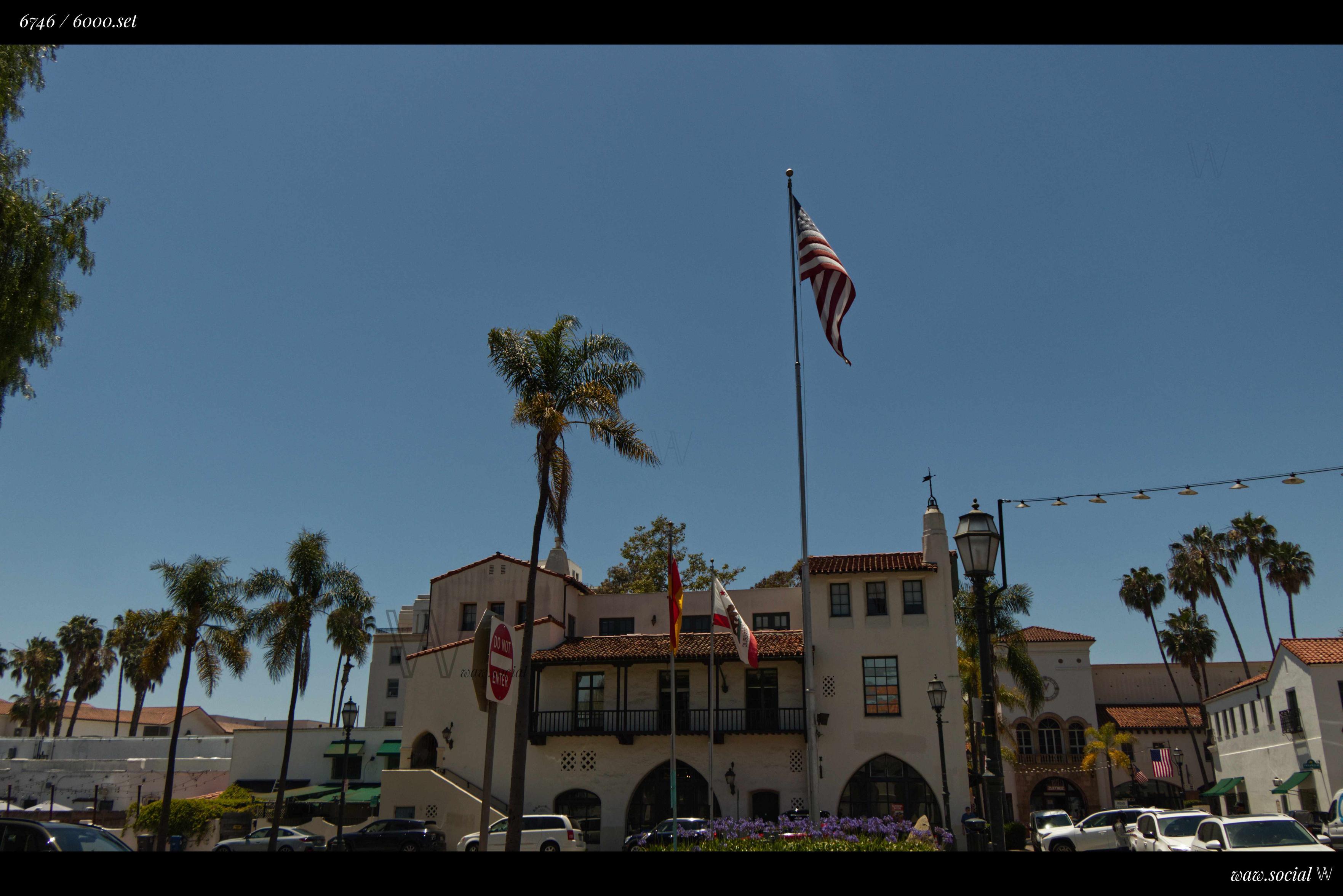 A warm color photo of a building in Downtown Santa Barbara, California with the US, California and Santa Barbara flag in frame.
