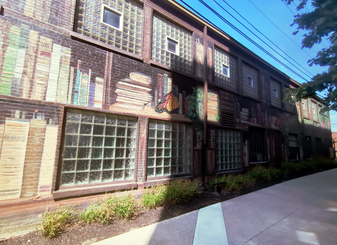 an alleyway where the wall, with glassblock windows, has been painted like a giant bookshelf