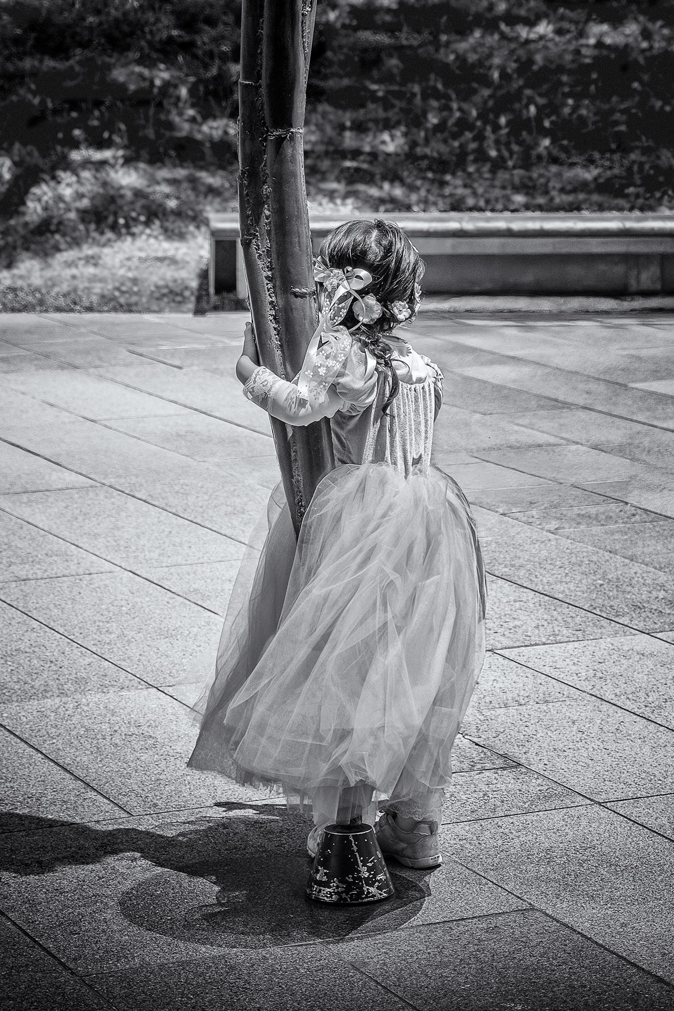 Young girl in princess dress holds onto the leg of a sculpture in the Roppongi Hills district of Tokyo, Japan.