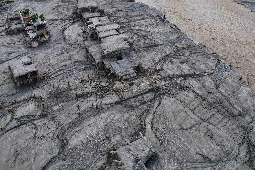 Rescue workers inspect damaged mud-covered structures.