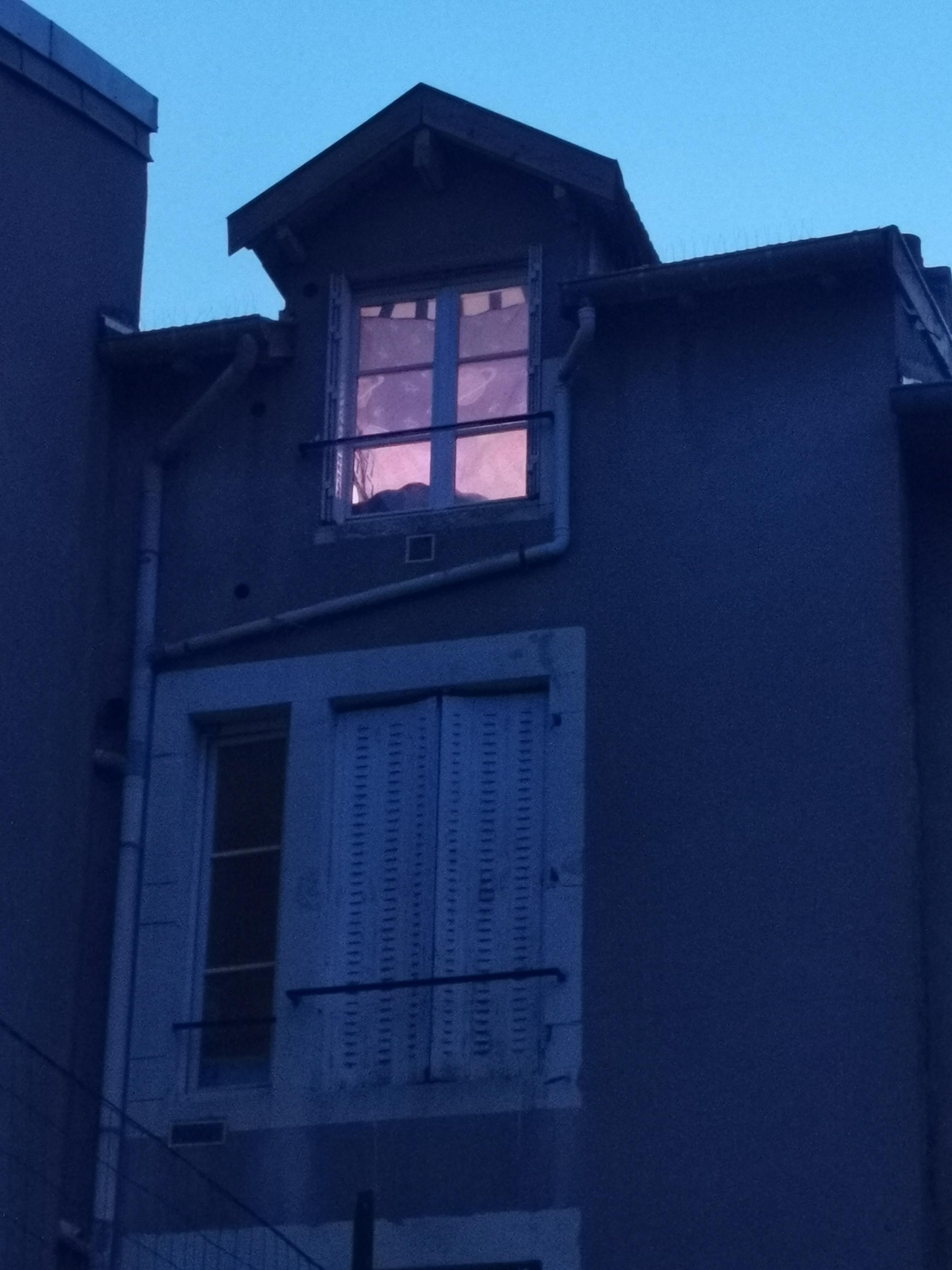 Le soir venu, vue côté cour sur un immeuble d'un quartier populaire, une fenêtre est éclairée.