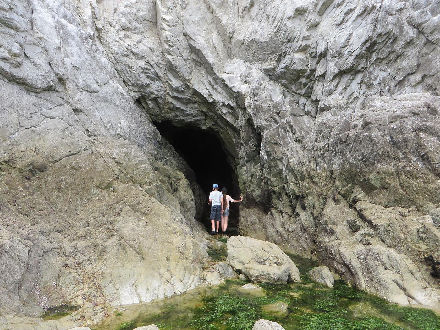 deux enfants de dos devant l'entrée d'une grotte dans un grand rocher