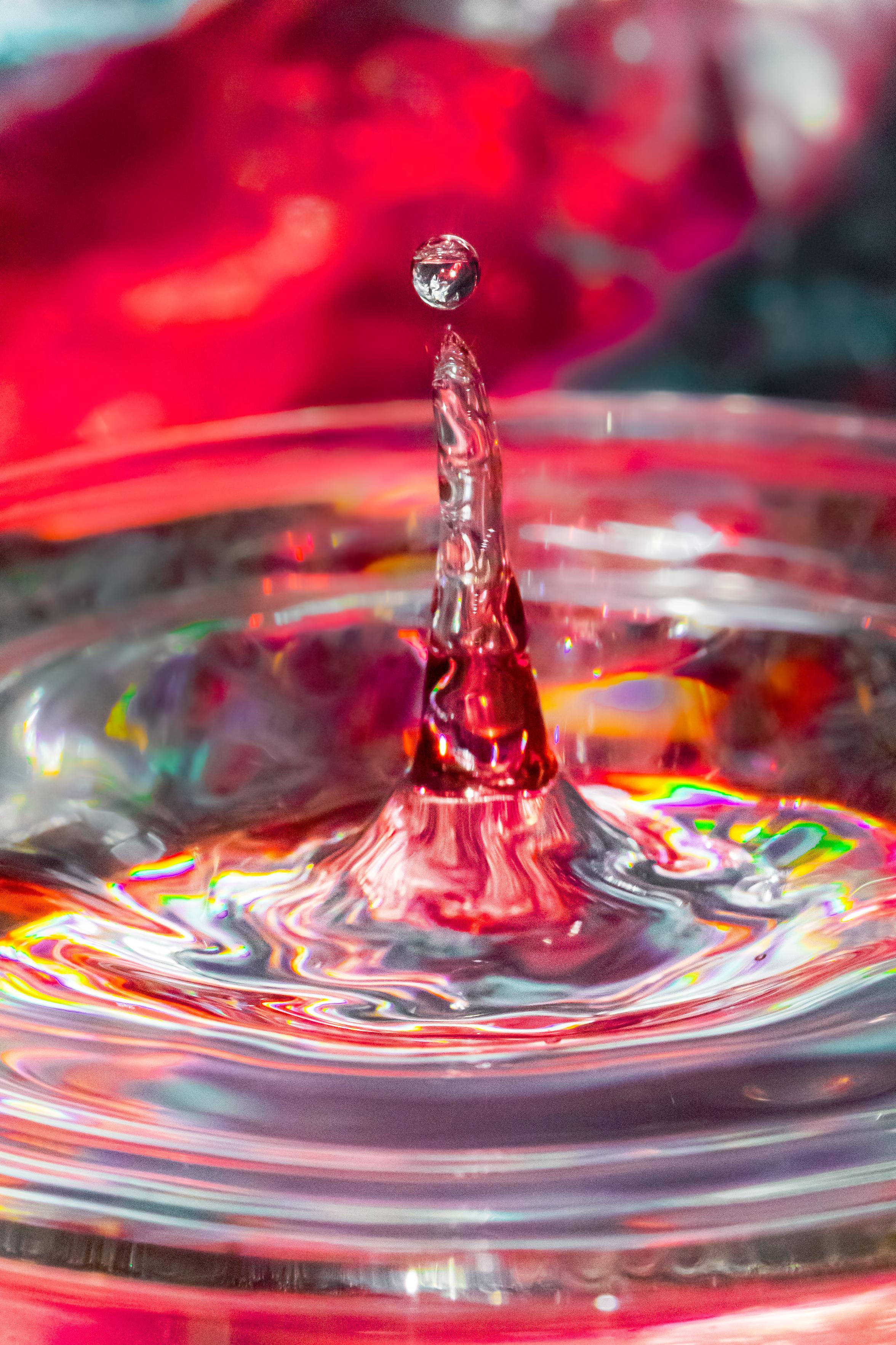 A pretty blurry close-up but bright and colourful photo of a water drop rising up from a wine glass.