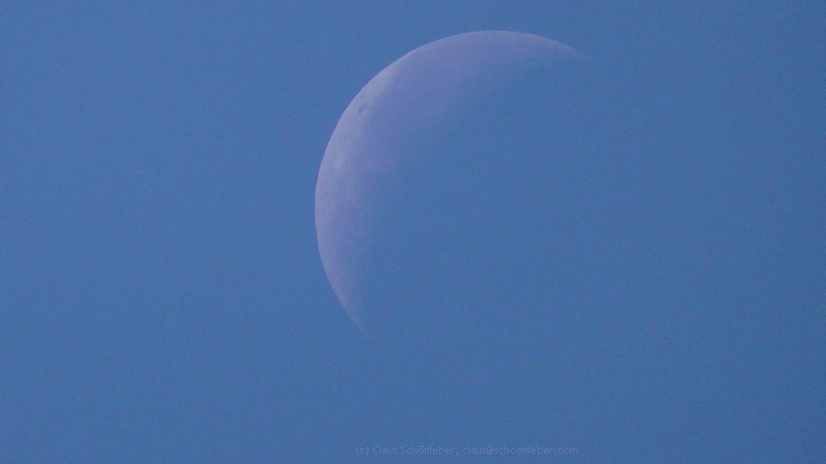 A daylight picture of the decrecend Moon, zoomed in at max., taken freehand.

The sky is deep blue, the grey-ish shadow-like, just partly seen moon is in the center of the picture, the left upper side is visible, the rest of it fades into the blue to the right lower side. Just the Moon in the sky.

On the visible part lefthand is the shadow of a crater. Not much more texture because of the bright sun lighing the sky.

The size of the picture is reduced.

Some EXIF Data:

Make - Panasonic
Model - HC-V180
ExposureTime - 1/750 seconds
FNumber - 4.20
MaxApertureValue - F 1.80
FocalLength - 103.00 mm
DigitalZoomRatio - 1.00 x
FocalLengthIn35mmFilm - 1740 mm