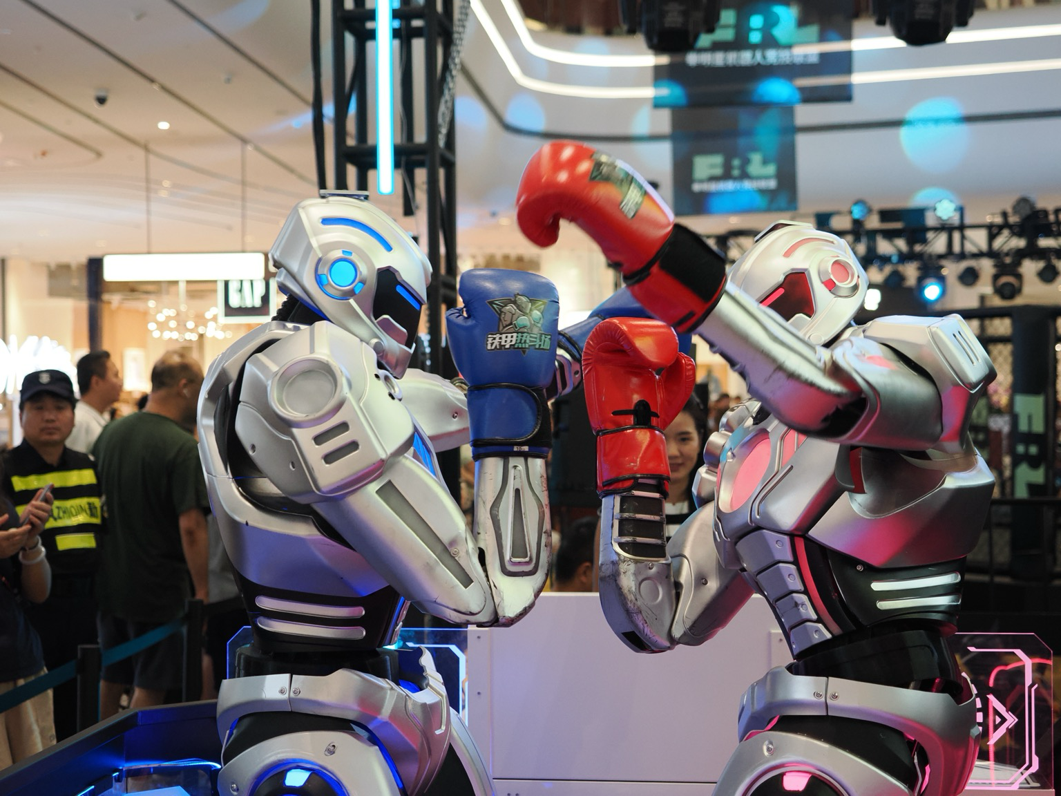 Two robots, one with red accents and red boxing gloves and one with blue accents and blue boxing gloves face each other. Both are trying to punch with their left hand