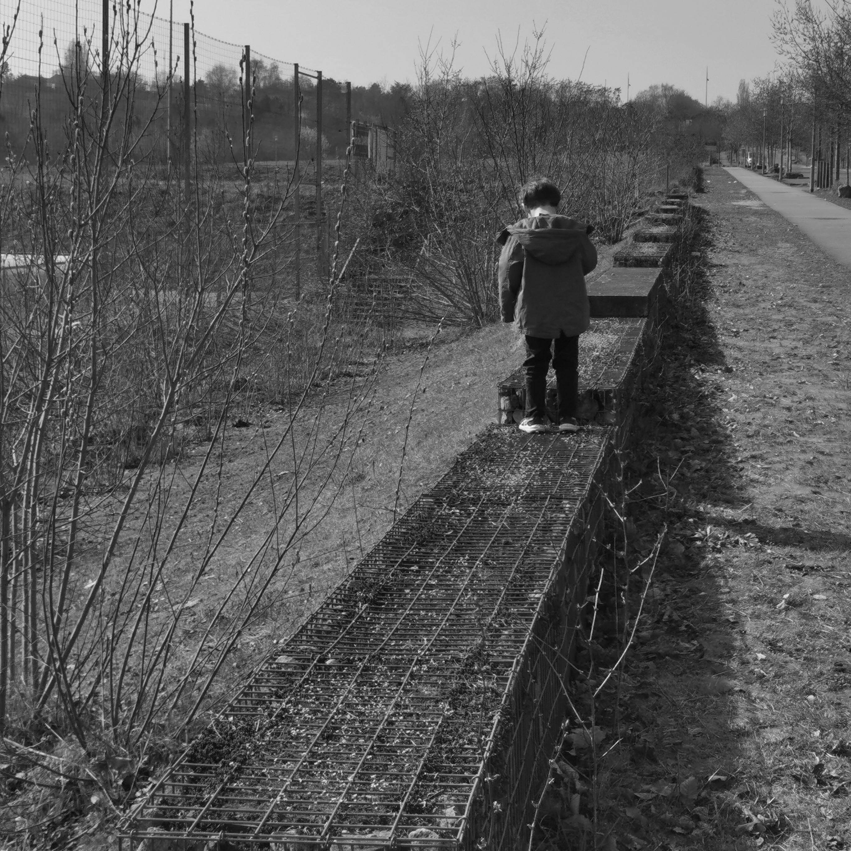 Sur un muret dans une zone encore largement en friche, un enfant teste son équilibre.