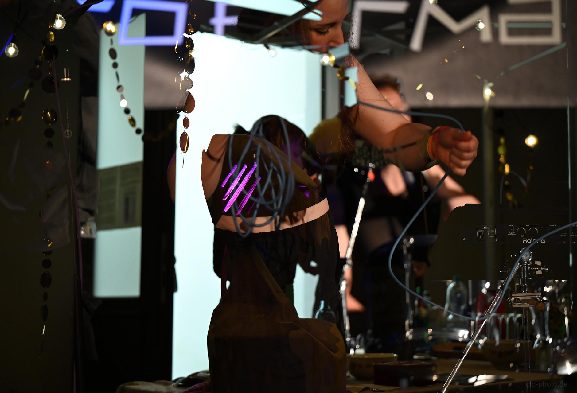 A layered, reflective shot of a performer surrounded by cables and electronic music gear, creating a dynamic, atmospheric scene with overlapping lights and textures.