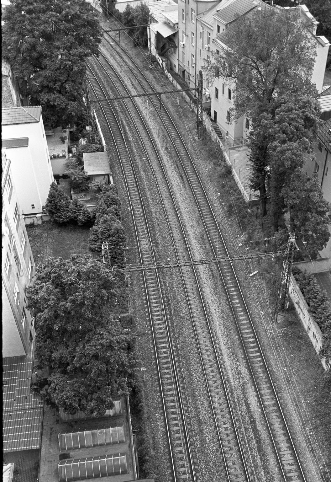 Aerial view of railway tracks curving through a residential area, surrounded by trees and buildings. The image is in black and white.