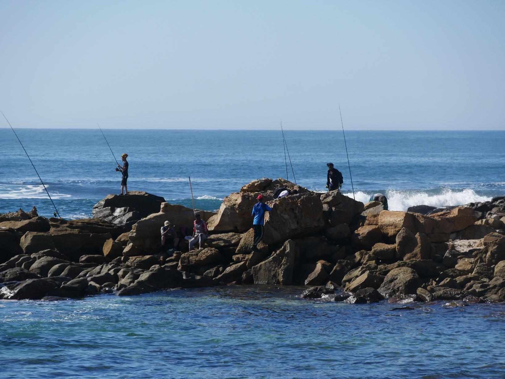 An der Küste von Mosselbay stehen Angler auf den rauhen Felsen und versuchen ihr Glück mit einem guten Fang. Südafrika 2022