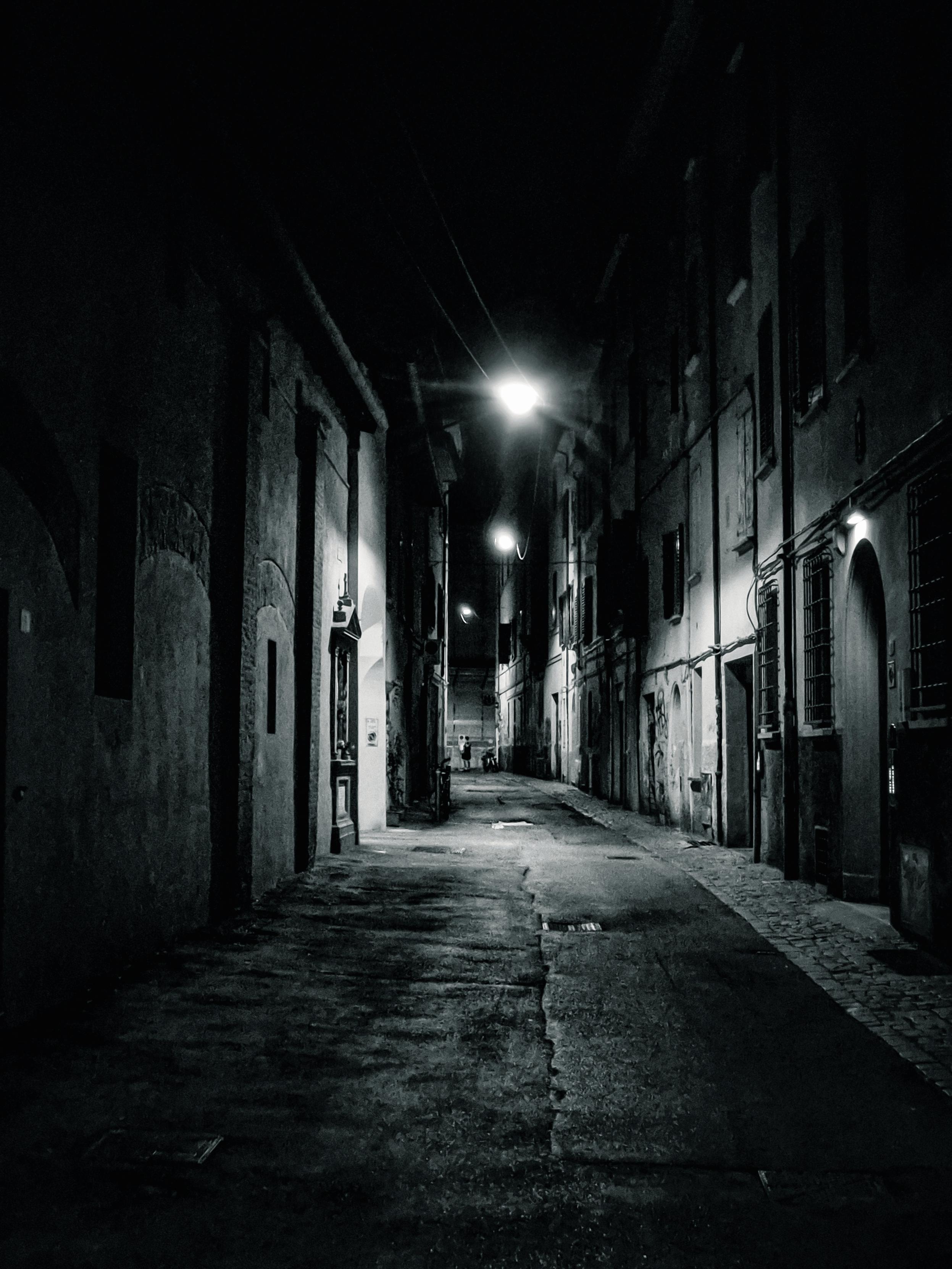 A black and white photo of a practically empty street at night in Bologna