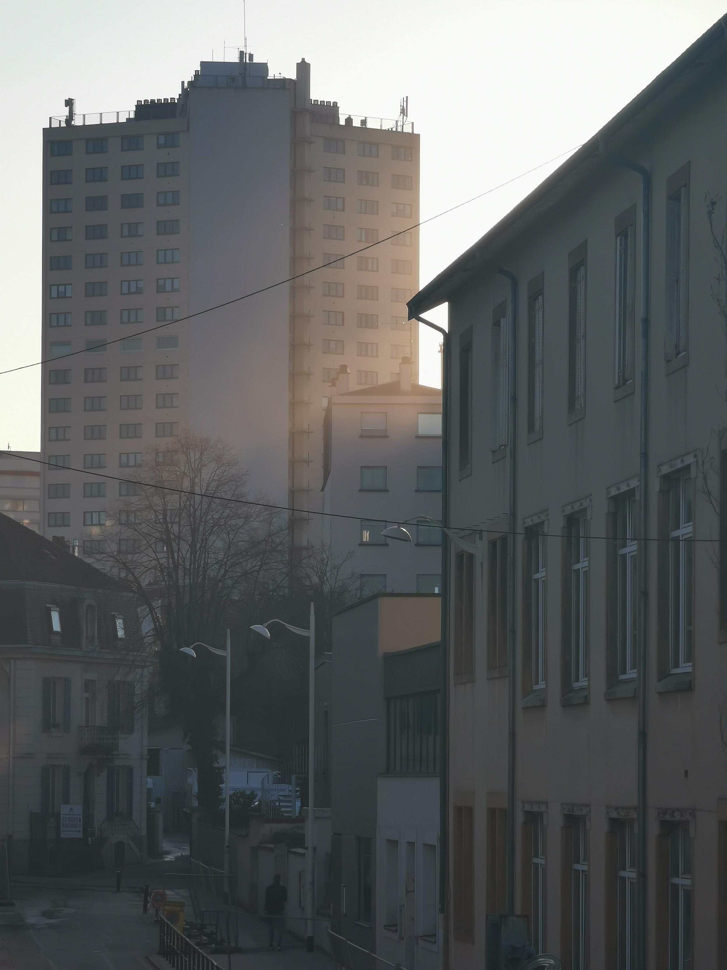 Fin de journée à Nancy, le soleil tombe oblique sur une tour dispersant la lumière et créant un halo au-dessus des rues plus sombres en contrebas