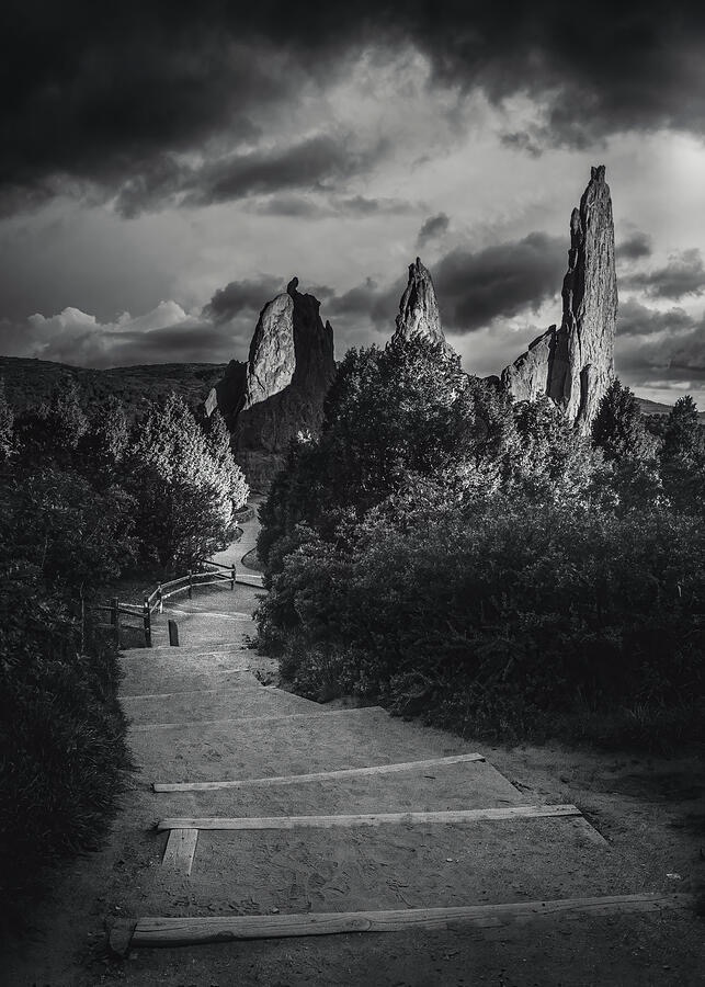 Black-and-white landscape photograph of a winding trail leading toward towering rock formations at Garden of the Gods in Colorado beneath dramatic storm clouds.
