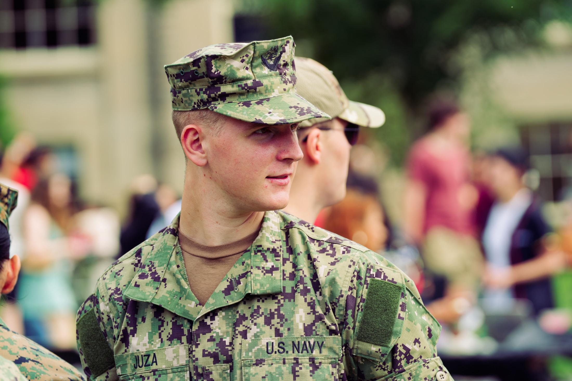 Man wears a digital camoflauge uniform reading JUZA and U.S. NAVY and looks to the right wearing a hat