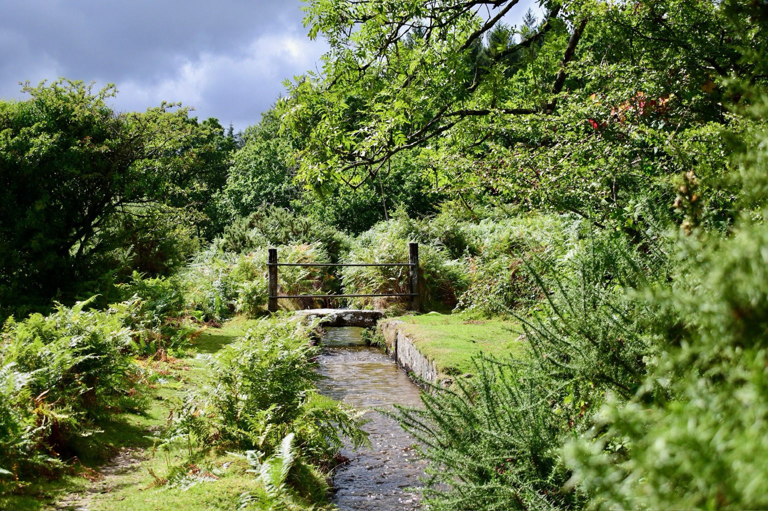 A stream and stone bridge under a cloudy sky.